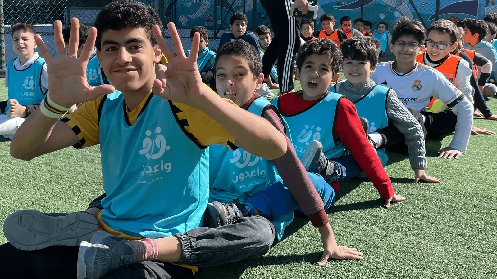 أبناء واعدون يجلسون على أرض الملعب ويلوّحون بفرح